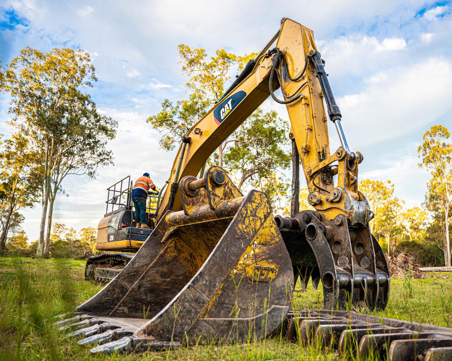 Low-angle view of an excavator bucket and grapple on grass