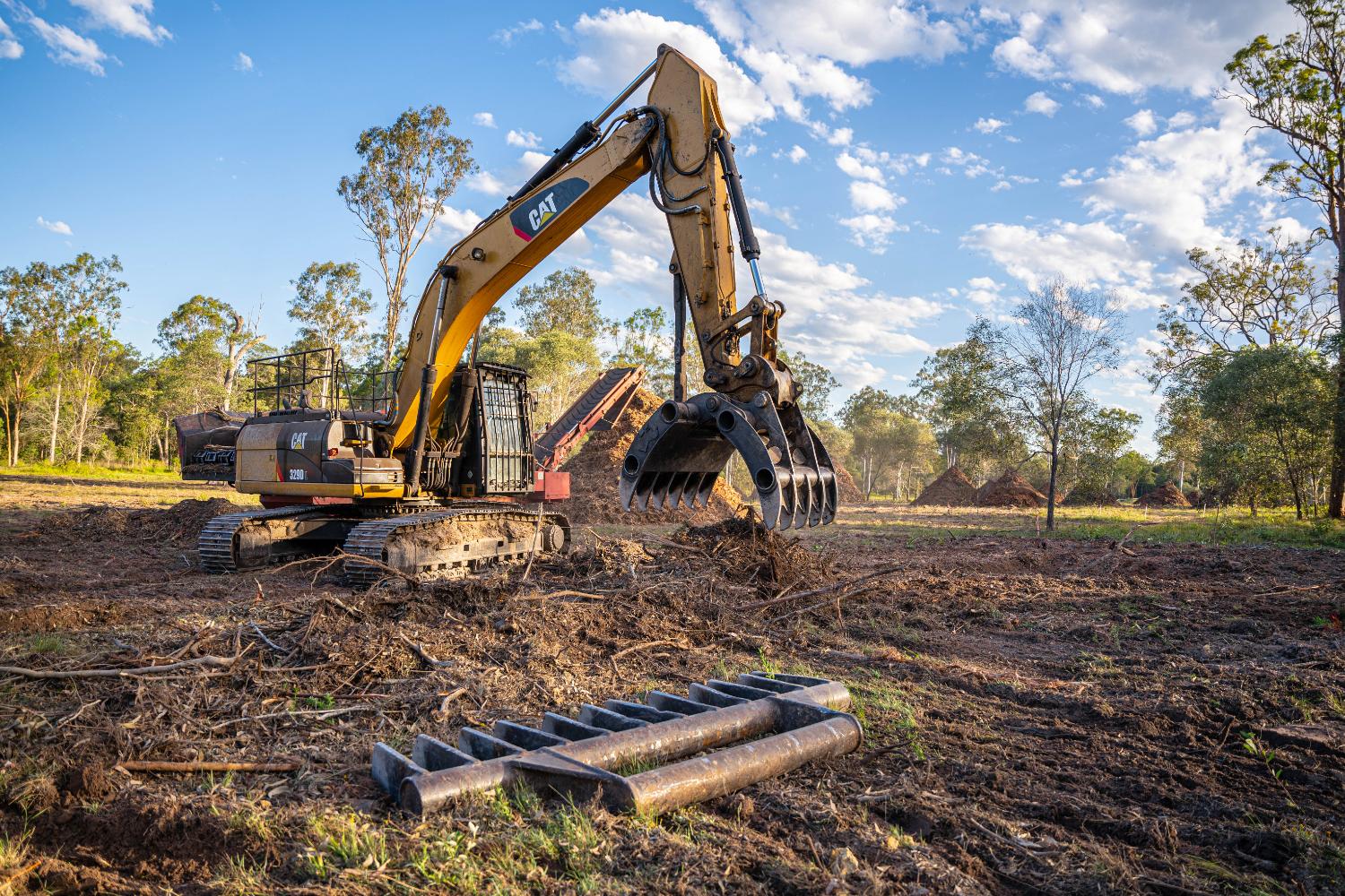 Excavator feeding a grinder with mulch piles behind